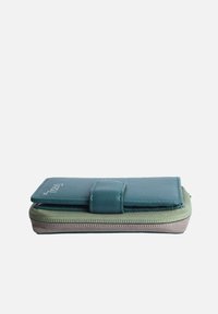 Folded wallet in teal leather with a snap closure, layered over a textured light green fabric base. Zippered edge with contrasting stitching.