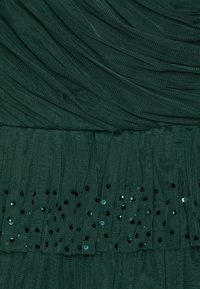 Tissu plissé vert foncé avec de petites paillettes noires et brillantes dispersées le long de la partie inférieure.