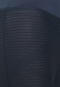 Leggings azul-marinho feitos de material elástico com textura canelada e detalhe de padrão geométrico; apresentam uma cintura lisa e costuras planas.