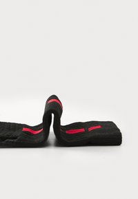 Textil negro con una superficie texturizada, que presenta franjas rojas horizontales. El material es flexible y se dobla en el medio.