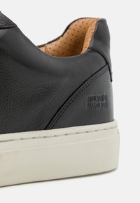 Černé kožené tenisky s texturovaným povrchem, krémovou gumovou podrážkou a perforovanou béžovou podšívkou. Disponují embosovaným logem na boku a minimalistickým designem.