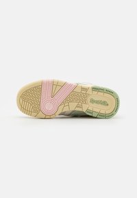 Suola della scarpa in gomma beige con accenti rosa e verde, con impugnature testurizzate, dettagli circolari e marchio "Spotbil" di lato.