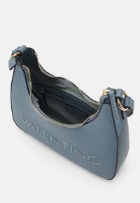 Μπλέ δερμάτινη τσάντα χειρός με φερμουάρ, ανάγλυφη γραφή και χρυσές λεπτομέρειες. Ο εσωτερικός χώρος περιλαμβάνει τσέπη με φερμουάρ.