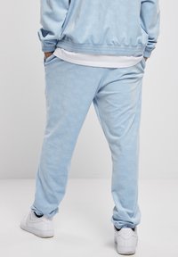Light blue tracksuit made of soft fabric, featuring a subtle pattern. Jogging pants have side pockets and elastic cuffs. Paired with white sneakers.