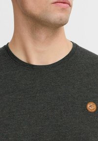 Donkergrijze t-shirt met korte mouwen en een ronde halslijn, gemaakt van gestructureerde stof. Heeft een klein, rond logo-embleem op de linkerkant van de borst.