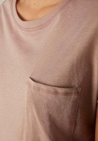 T-shirt a maniche corte di colore rosa chiaro, realizzato in materiale morbido, con taschino sul petto e dettagli di cucitura abbinati. Tessuto liscio, scollatura rotonda.