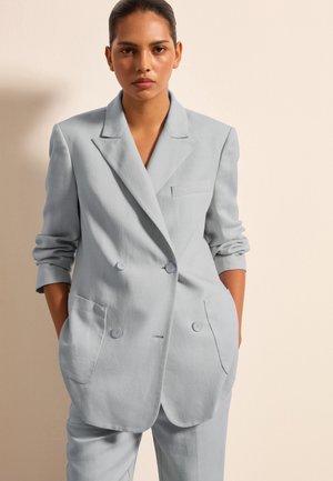 Blazer azzurro chiaro doppiopetto con bavero a punta, due grandi tasche frontali e maniche leggermente arrotolate. Tessuto liscio e texturizzato.