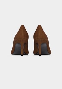 Καφέ σουέντ ψηλοτάκουνα παπούτσια, βλέποντας από πίσω, με λεπτούς τακούνια και μαύρες σόλες σε λευκό φόντο.