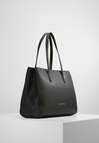 Černá kožená taška přes rameno s dvěma uchy, charakterizovaná strukturovaným designem a zlatým logem. Hladká textura a minimalistický styl.
