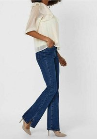 Hvid, prikket bluse med flæse i halsen, parret med mørkeblå, svajede jeans med sideslids. Lysebrune spidse hæle fuldender outfittet.