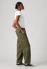 Weißes kurzärmeliges T-Shirt kombiniert mit lockeren olivgrünen Cargo-Hosen mit mehreren Taschen und elastischen Bündchen, getragen mit schwarzen Sneakers.