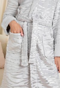 Accappatoio grigio in peluche con un motivo a strisce di zebra e una leggera lucentezza. Presenta una vita con cordone, una texture morbida e due tasche frontali.