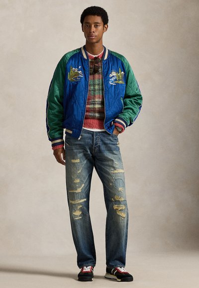 Modna bombažna jakna v modri in zeleni barvi z vezenimi prizori, nošena preko večbarvnega črtastega puloverja. Obrabljene modre kavbojke in črni čevlji.