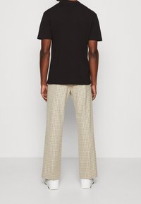 Black cotton short-sleeve t-shirt paired with beige checkered wide-leg pants and white sneakers, viewed from the back.
