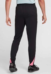 Juodos laisvalaikio kelnės su elastinga juosmens juosta, prigludusiu dizainu ir rožiniais akcentais prie čiurnos. Dėvimos su juodais sportiniais bateliais.