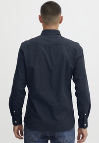 Temno modra srajca z dolgimi rokavi, s koničastim ovratnikom, gumbi na manšetah in gladko teksturo. Opazno šivanje in slim fit dizajn.