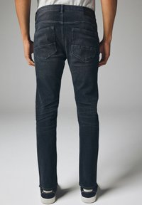 S�ötétkék farmernadrág, slim fit fazonban, öt zsebbel és finom varrási részletekkel. A hátsó részen két folt zseb található, valamint sima derékrész.