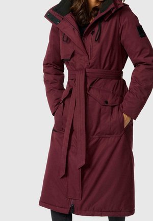 Długi bordowy płaszcz z paskiem, dużymi przednimi kieszeniami i kapturem. Posiada kontrastujący czarny kołnierz i fakturowaną tkaninę. Zamek błyskawiczny i ozdobne guziki.