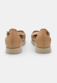 Zapatos de cuero marrón con diseño abierto, correa con hebilla y suela de goma beige baja. El acabado texturizado en la parte superior realza el interés visual.