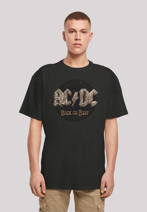 Black cotton t-shirt featuring a distressed AC/DC logo with "Rock or Bust" in gold, short sleeves, and a relaxed fit.