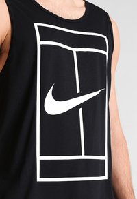 Canotta nera senza maniche in cotone, con un grande logo bianco Nike e un design geometrico sulla parte frontale. Texture liscia.
