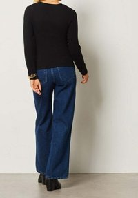 Haut noir à manches longues associé à un jean bleu taille haute à jambes larges. La tenue présente un design simple et des couleurs unies, avec une texture lisse.