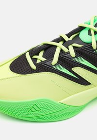 Limegrønne og sorte atletiske sko med mesh-overdel, teksturerede accenter, flade snørebånd og fiskebensmønster på sålen.