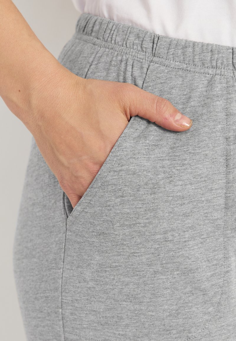 Käsi le repose dans la poche d'un pantalon de survêtement gris, montrant la texture du tissu et la ceinture élastique au-dessus.