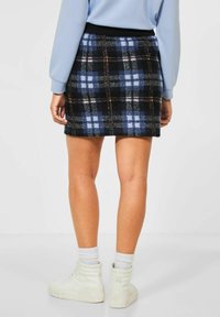 Jupe mini à carreaux dans des nuances de bleu foncé, noir et bleu clair. Fabriquée en tissu doux, elle présente une taille élastique noire et une finition texturée.