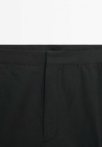 Czarne spodnie o gładkim, matowym wykończeniu. Posiadają płaski pas i subtelne detale szycia. Czysty design, bez widocznych kieszeni czy zdobień.