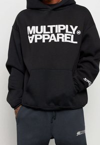 Felpa con cappuccio nera realizzata in tessuto morbido, con grande logo bianco "MULTIPLY APPAREL" sulla parte anteriore e tasca a marsupio. Dettagli sulle maniche.