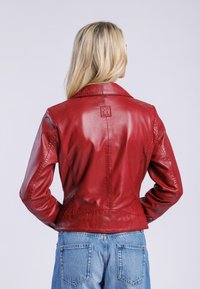 Červená kožená bunda s přiléhavým střihem, s klopovým límcem a embosovaným detailem loga. Hladká textura a čisté švy.