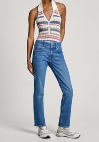 Randig ärmlös topp med krage i blått, rött och grönt, kombinerad med ljusblå raka jeans och grå sneakers.