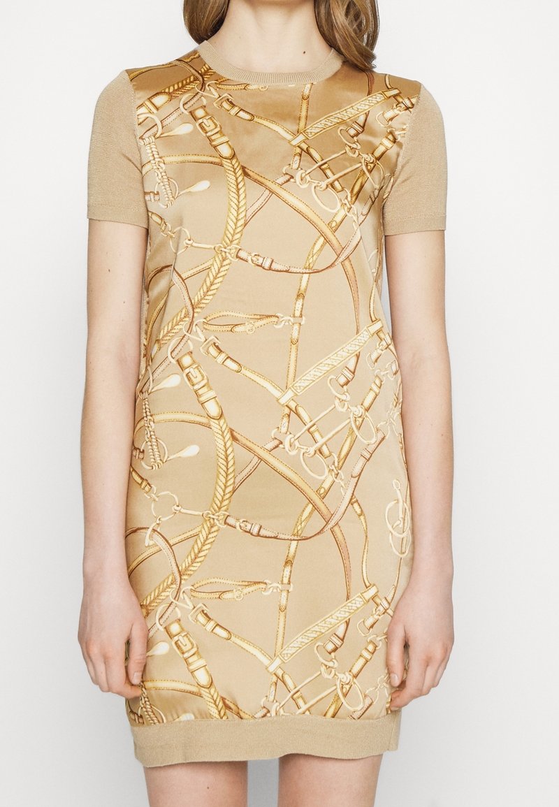 Robe beige présentant un design brillant et à motifs de cordes et de détails en matériel, avec des manches courtes et un col en rib. Texture douce.
