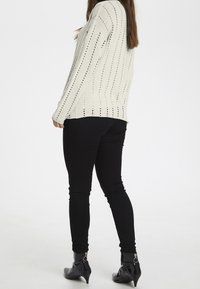 Light beige knitted sweater with vertical openwork pattern, paired with black skinny jeans and ankle boots with zipper details.