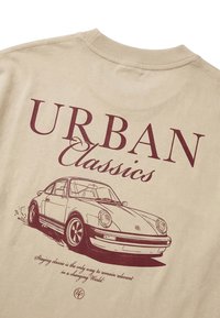 Μπεζ πουκάμισο με μπορντό κείμενο «URBAN Classics» και λεπτομερή σκίτσο κλασικού αυτοκινήτου από κάτω, καθώς και ένα μικρό γραφικό απόσπασμα στο κάτω μέρος.