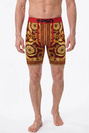 Mann trägt rot-gold gemusterte Boxershorts mit PSD-Logo am Bund, steht barfuß vor weißem Hintergrund.