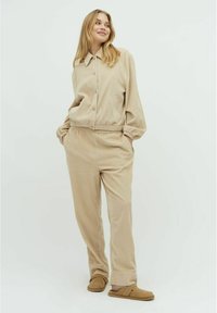 Beiges Corduroy-Loungewear-Set mit einem kragenlosen Knopf-Oberteil und elastischem Bund an der Hose, ausgestattet mit seitlichen Taschen und weichem Material.