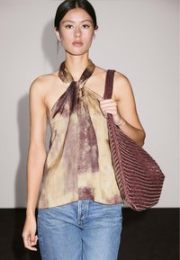 Lehký uzlový halter top v přírodních tónech a abstraktních vzorech, spárovaný s vysokými modrými džínami a v rámci s opletenou burgundskou kabelkou na rameno.