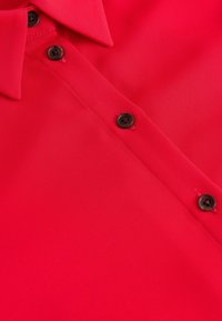 Chemise rouge vif avec un col pointu et trois boutons foncés fermés le long de la patte de boutonnage frontale.