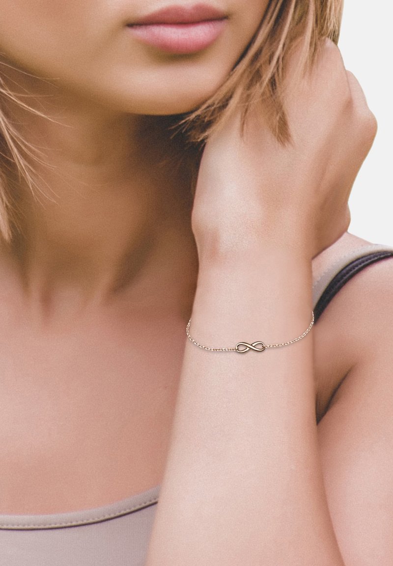 Silver chainarmband med ett oändlighetssymbol i centrum, med en slät, polerad yta och delikata länkar.