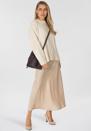 Maglione a maglia beige chiaro, gonna lunga in satin crema, scarpe con tacco color nude e una borsa in pelle marrone scuro con chiusura a coulisse.
