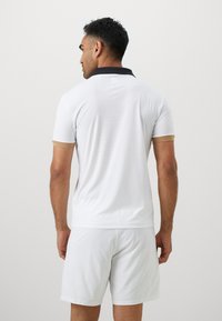 Weißes kurzärmliges Poloshirt mit schwarzem Kragen und hellbraunen Akzenten an den Ärmeln. Glatter Stoff mit feiner Textur. Legere Passform.