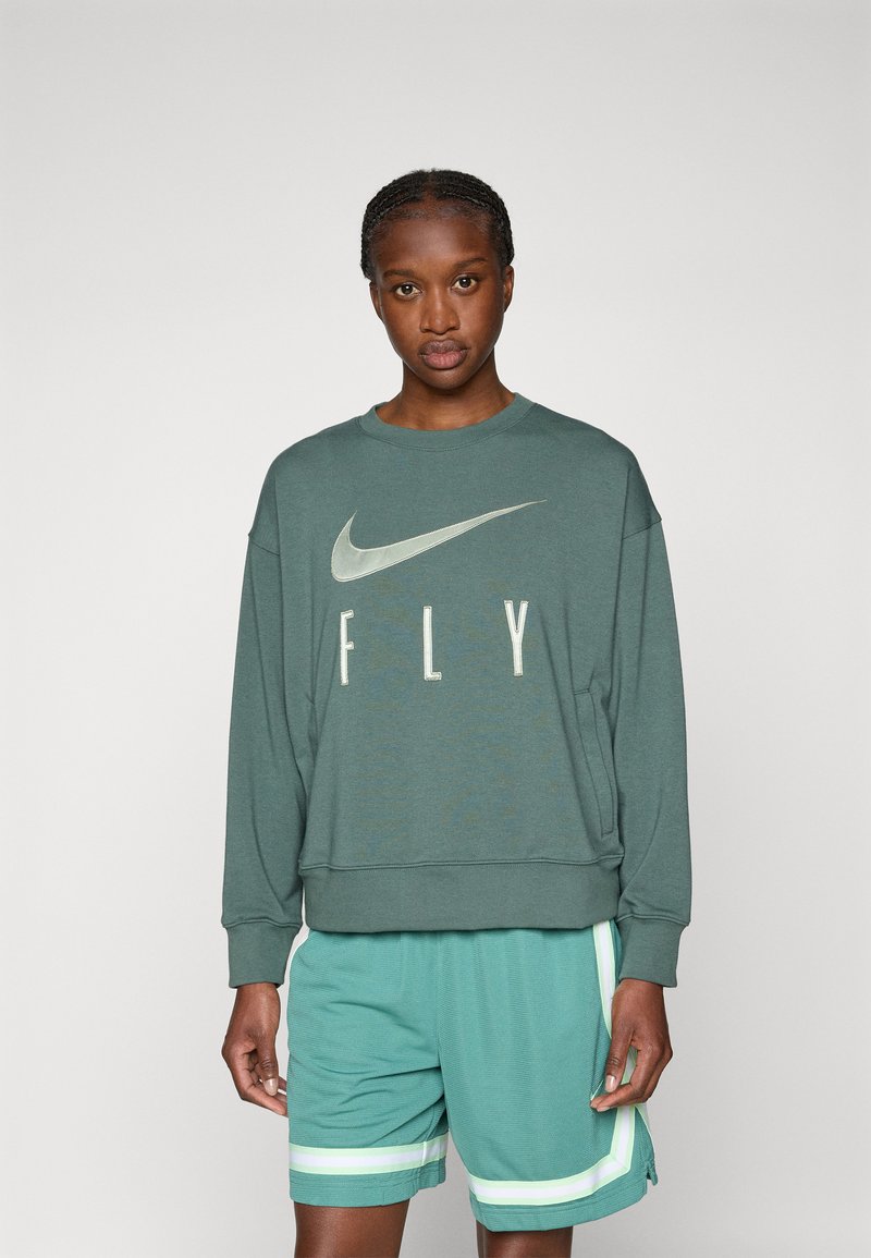Felpa a maniche lunghe di un verde scuro con il testo "FLY" e il logo swoosh di Nike. Abbinata a pantaloni corti color teal con accenti a strisce bianche e verdi.