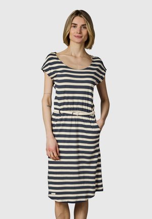 Nainen, jolla on polvenmittainen laivastonsininen ja valkoinen vaakaraitainen mekko, jossa on lyhyet hihat ja valkoinen kudottu vyö, seisoo käsi taskussa.