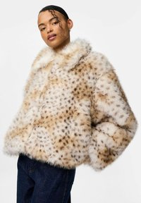 Cappotto in pelliccia sintetica con un motivo a stampa animale in crema e marrone chiaro, caratterizzato da un ampio colletto e una silhouette oversize, indossato con jeans scuri.