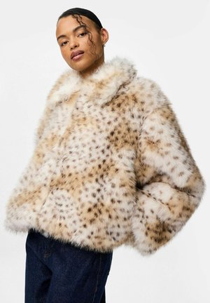 Cappotto in pelliccia sintetica con un motivo a stampa animale in crema e marrone chiaro, caratterizzato da un ampio colletto e una silhouette oversize, indossato con jeans scuri.