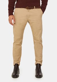 Kaki chinos, slim fit, tillverkade av bomullstyg. Matchade med ett brunt bälte och svarta läderstövlar. Uppvikta fållar, utan synliga mönster.