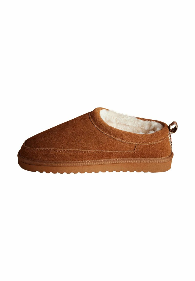 Brune ruskindsstof slippers med en blød, hvid pelsforing, rund tå og struktureret gummisål, der har en løftestrop bagpå for nem påtagning.