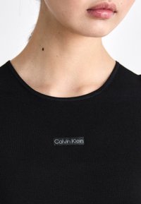 Zwarte ribstof shirt met een ronde halslijn, voorzien van een doorzichtige label met "Calvin Klein" in het wit gedrukt.